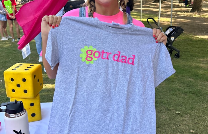 Marketing and Outreach Intern, Emma, holds up a "GOTR Dad" shirt 